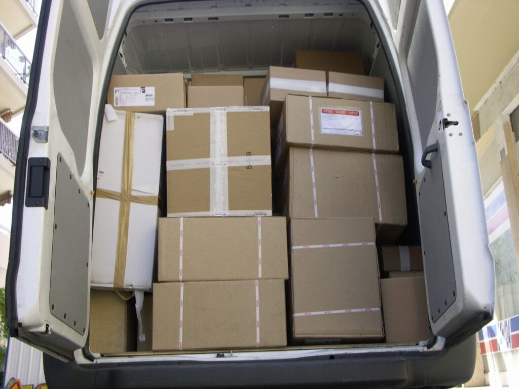 A van with its back doors open reveals a tightly packed load of various sized cardboard boxes, stacked nearly to the roof—ready for urgent delivery by a reliable same day courier.